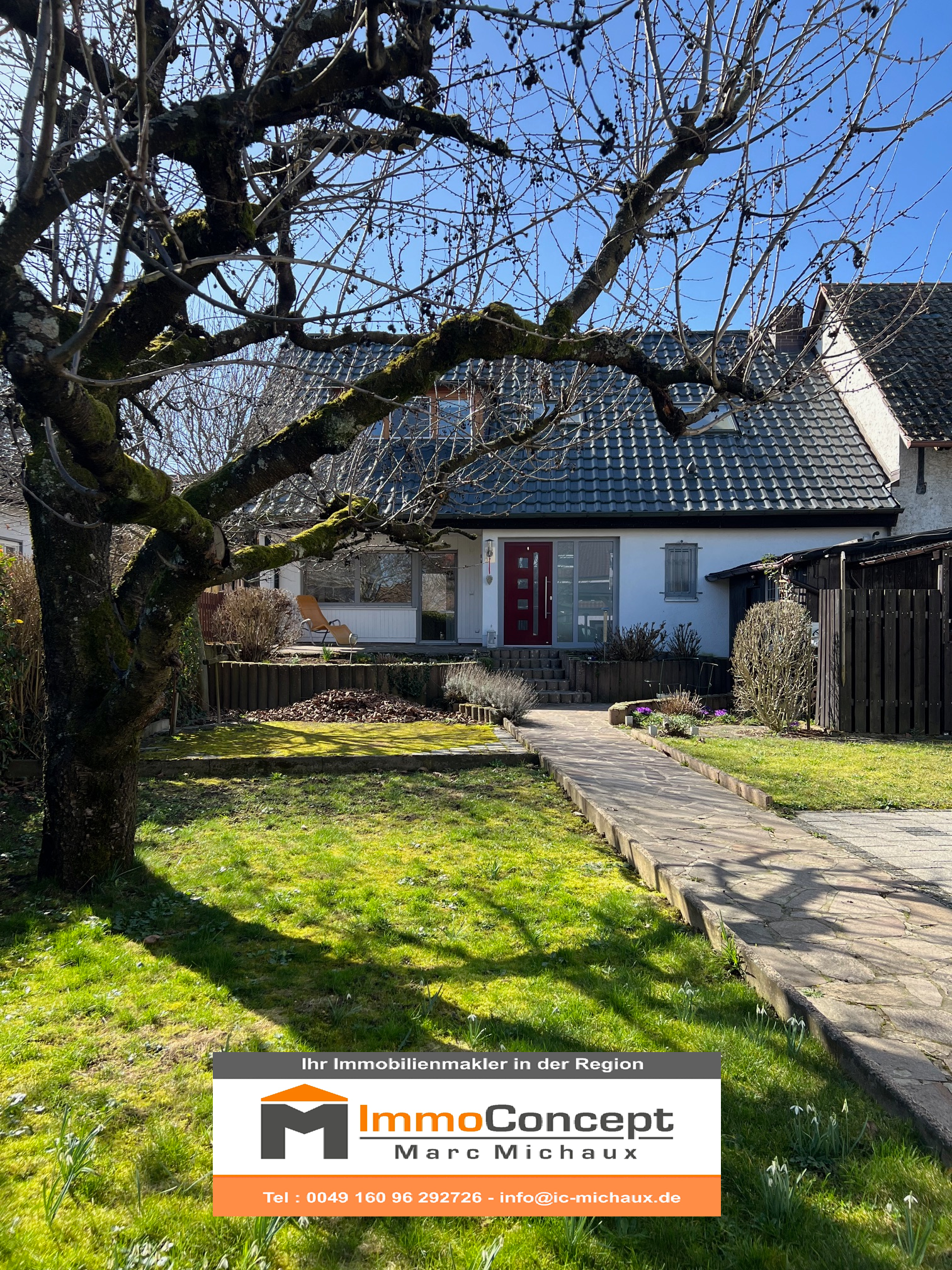 Weißes Gebäude mit rotem Dach, Balkonen und grünen Bäumen. Im Hintergrund ein Berg.