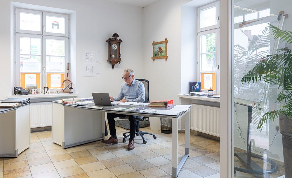 Ein Mann sitzt in einem Büro an einem Schreibtisch und benutzt einen Laptop.