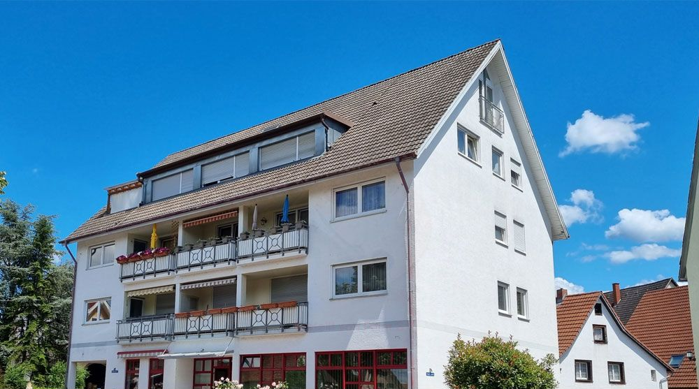 Modernes weißes Apartmentgebäude mit Balkonen unter blauem Himmel, unten prangt das Markenbanner von ImmoConcept.