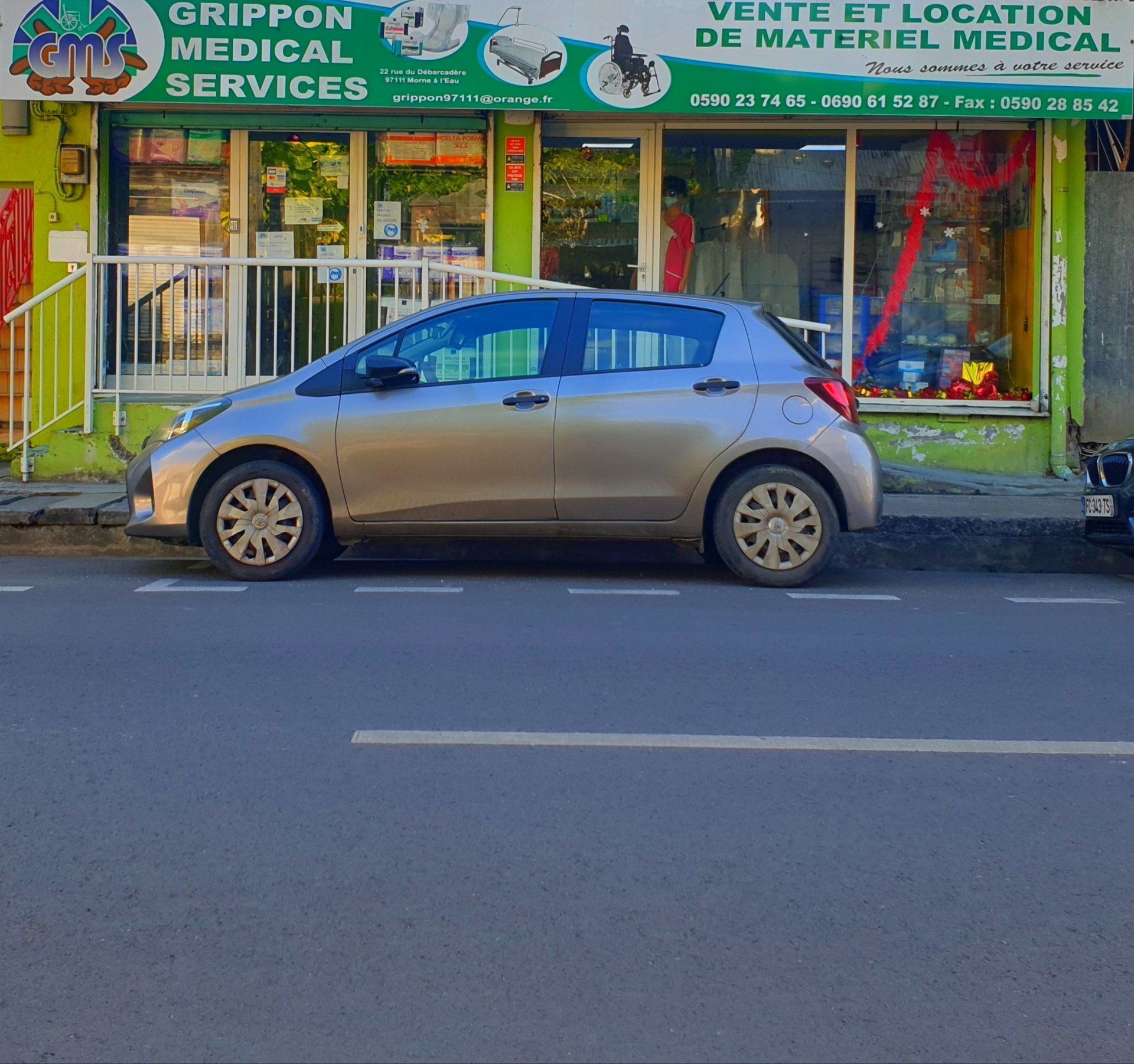 Une voiture à hayon argentée est garée devant la vitrine d'un magasin Grippon Medical Services.