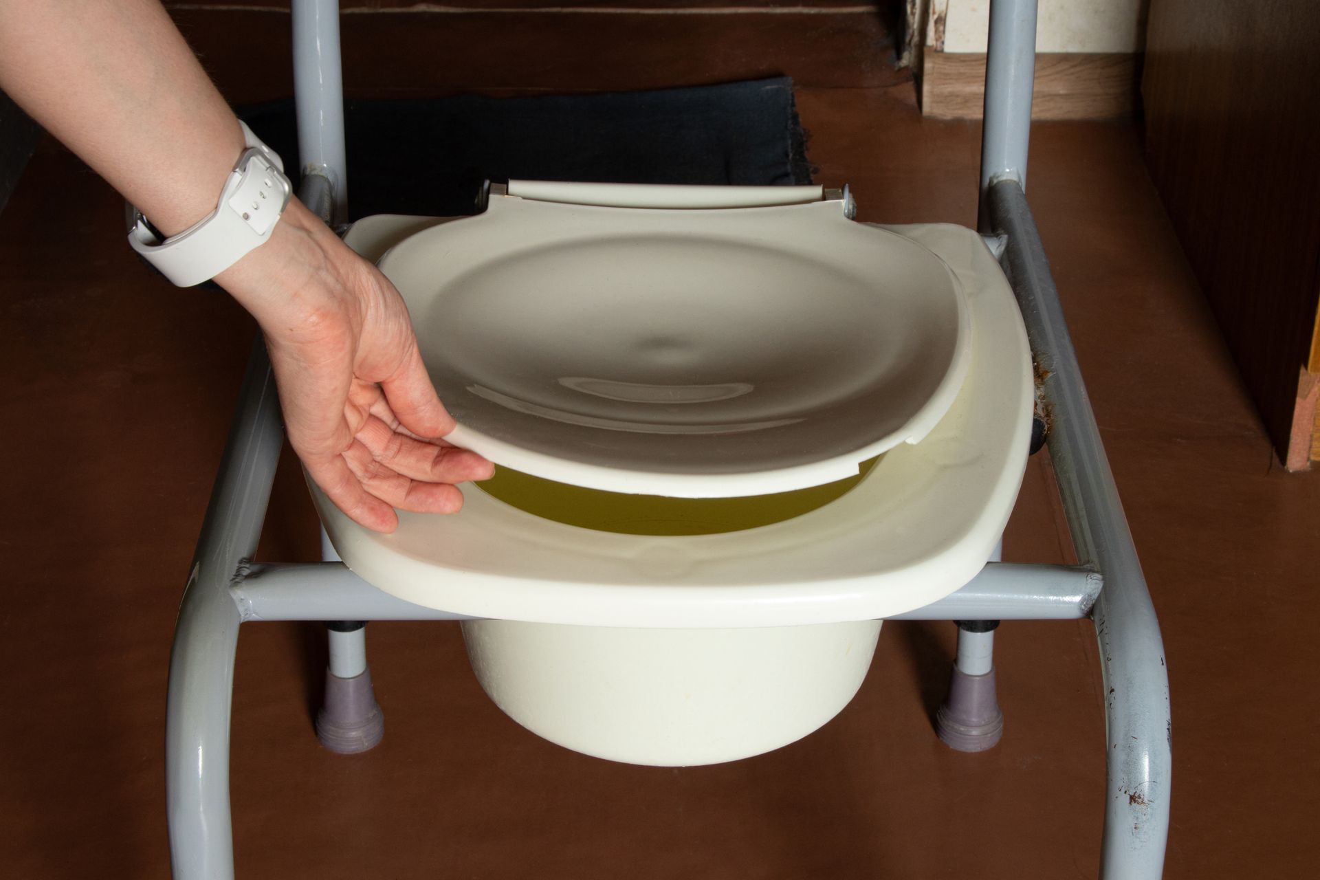 Une main referme le rabat d'une chaise percée.