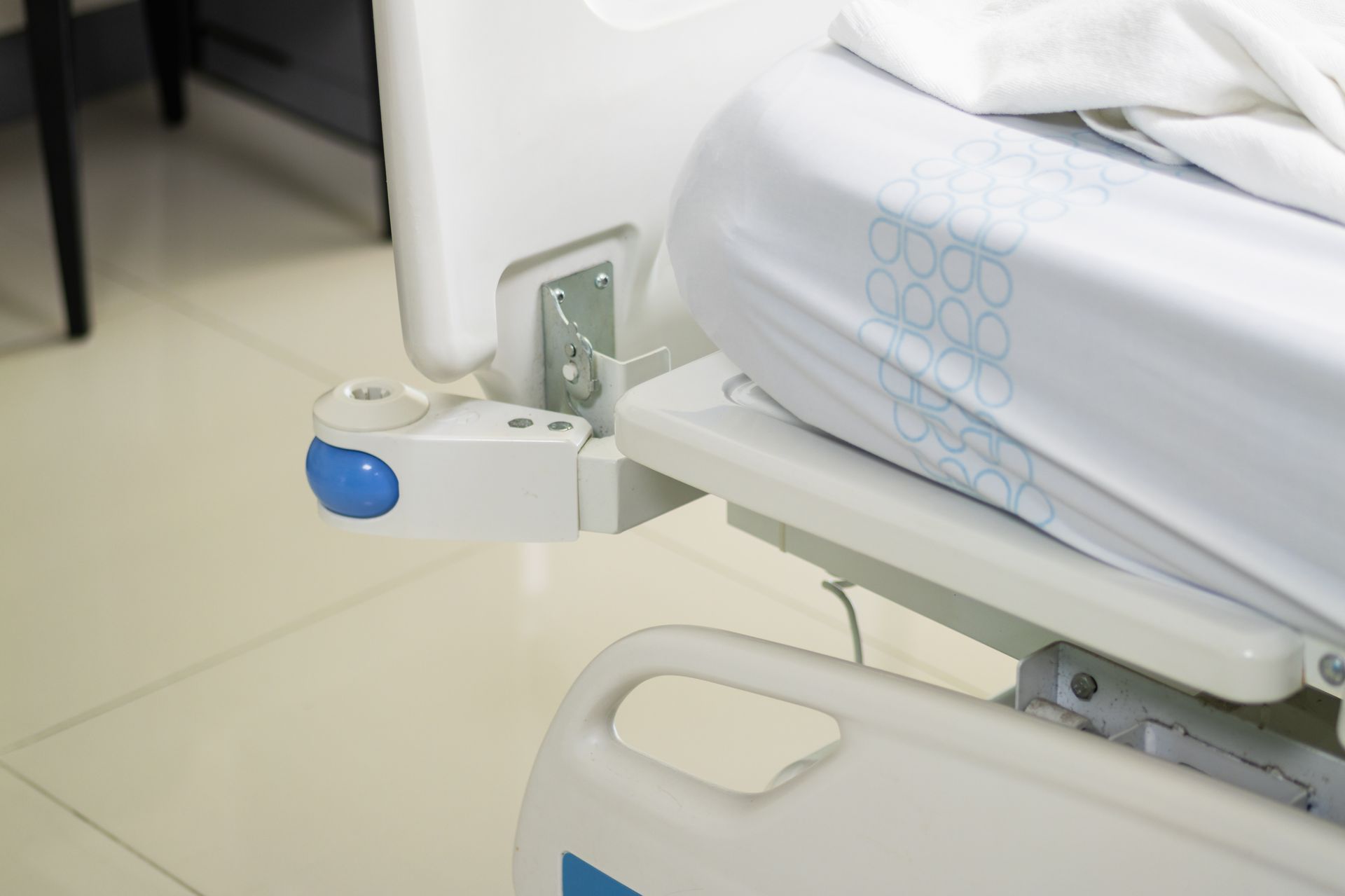 Barrière de lit médicalisé avec loquet bleu à côté d'un matelas blanc dans une chambre d'hôpital.