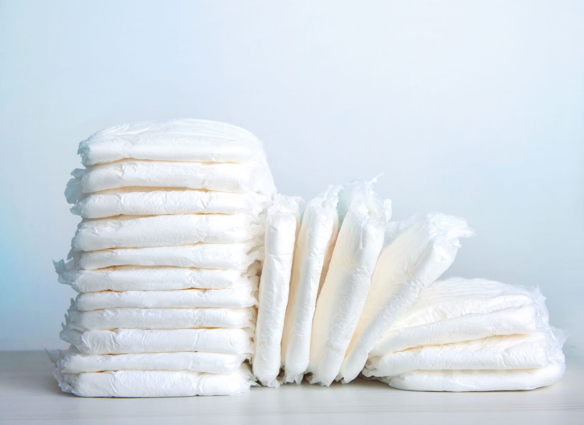 Serviettes hygiéniques blanches empilées sur fond bleu clair.