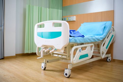Lit d'hôpital vide avec des draps bleus et une barrière de sécurité blanche dans une chambre lumineuse.