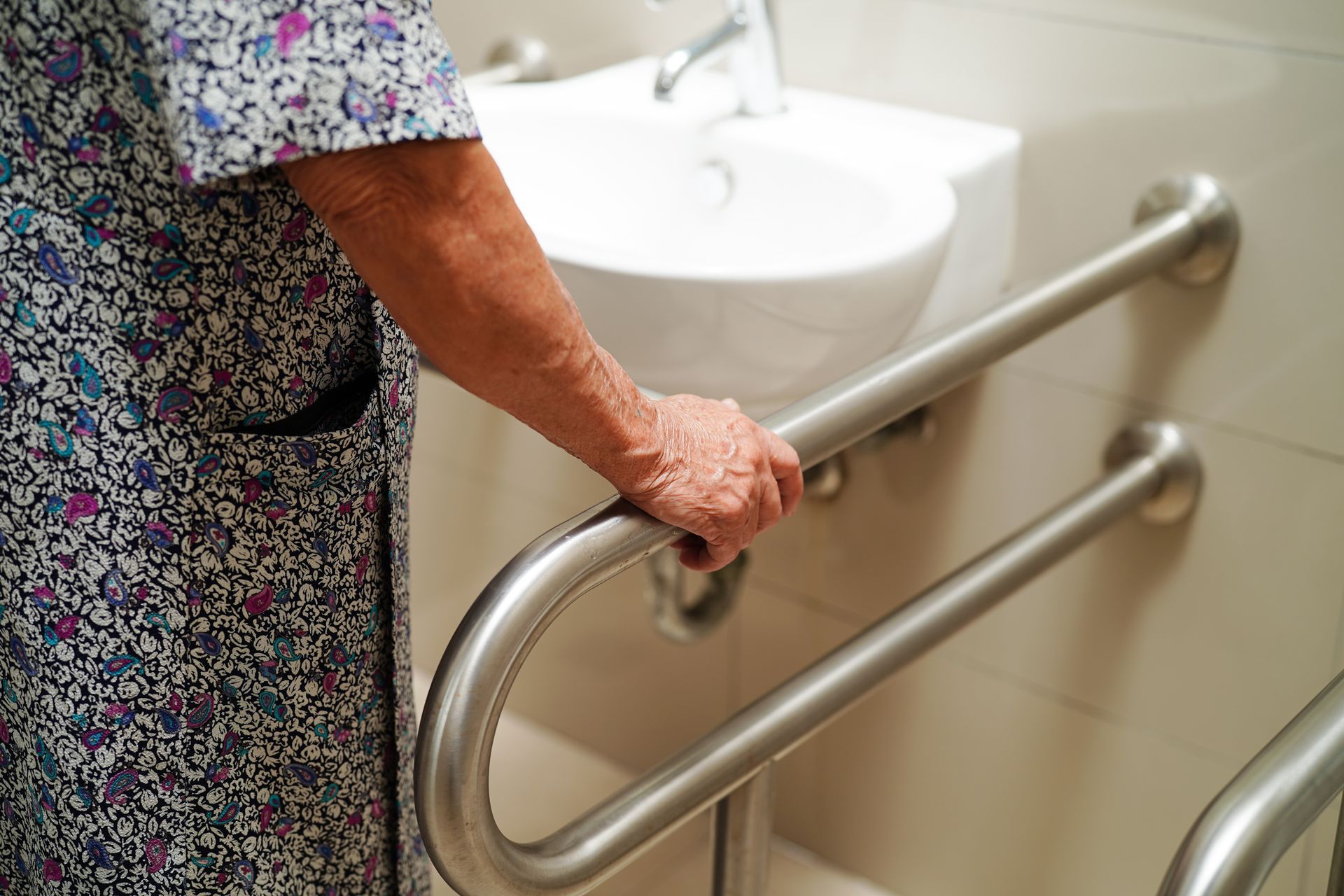 Une personne âgée se tient à une barre d'appui de salle de bains, à côté des toilettes.