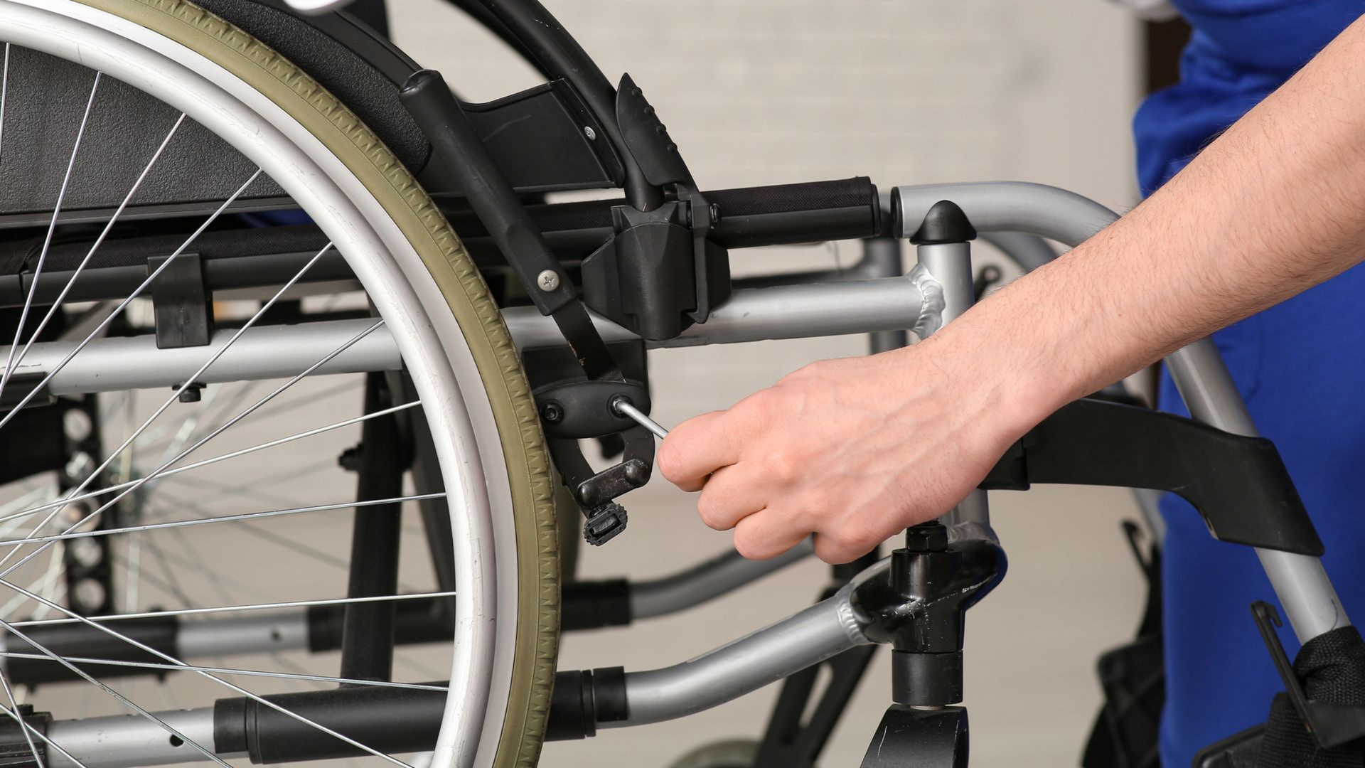 Un soignant en blouse bleue règle les roues d'un fauteil roulant.