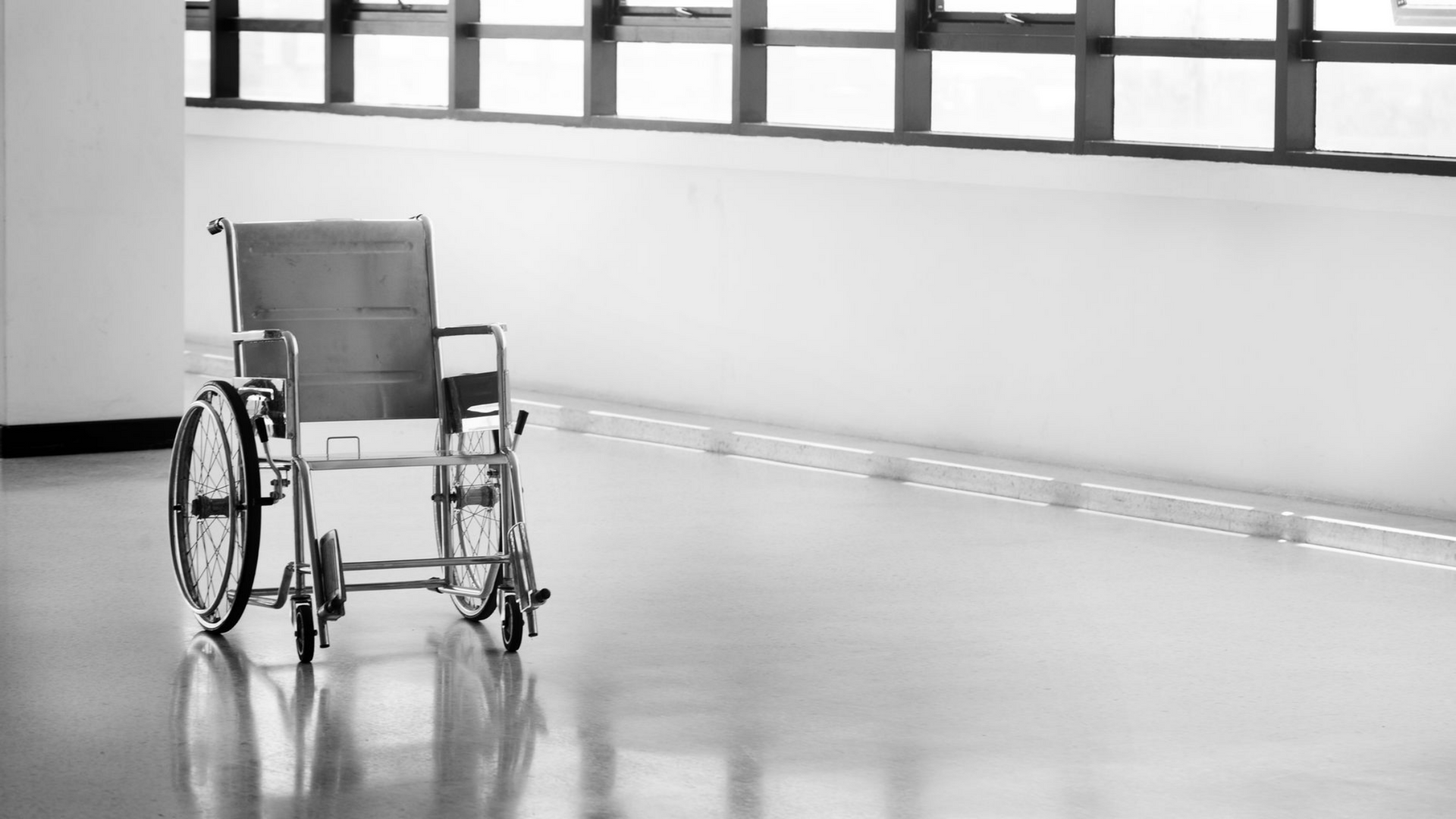 Fauteuil roulant dans un couloir lumineux avec de grandes fenêtres et un sol réfléchissant.