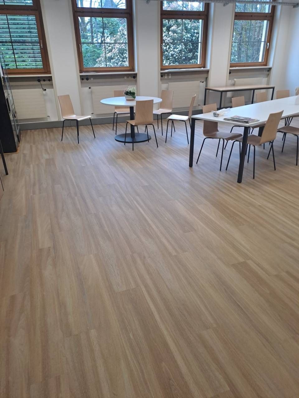 Une grande pièce avec parquet et tables et chaises.