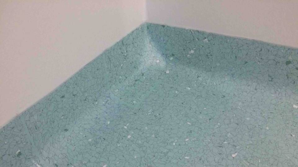 Un coin d'une pièce avec un sol vert et un mur blanc.