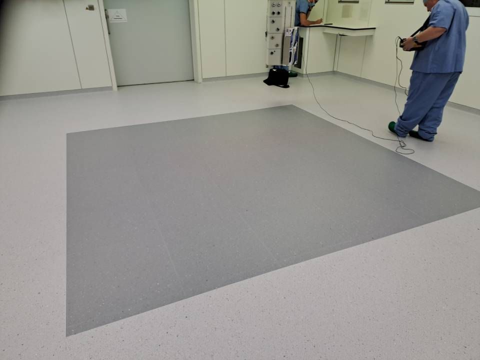 Deux hommes en tenue médicale se tiennent dans une pièce au sol gris.