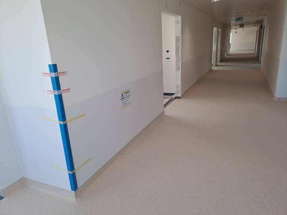 Un long couloir avec des murs blancs et un poteau bleu dans le coin.