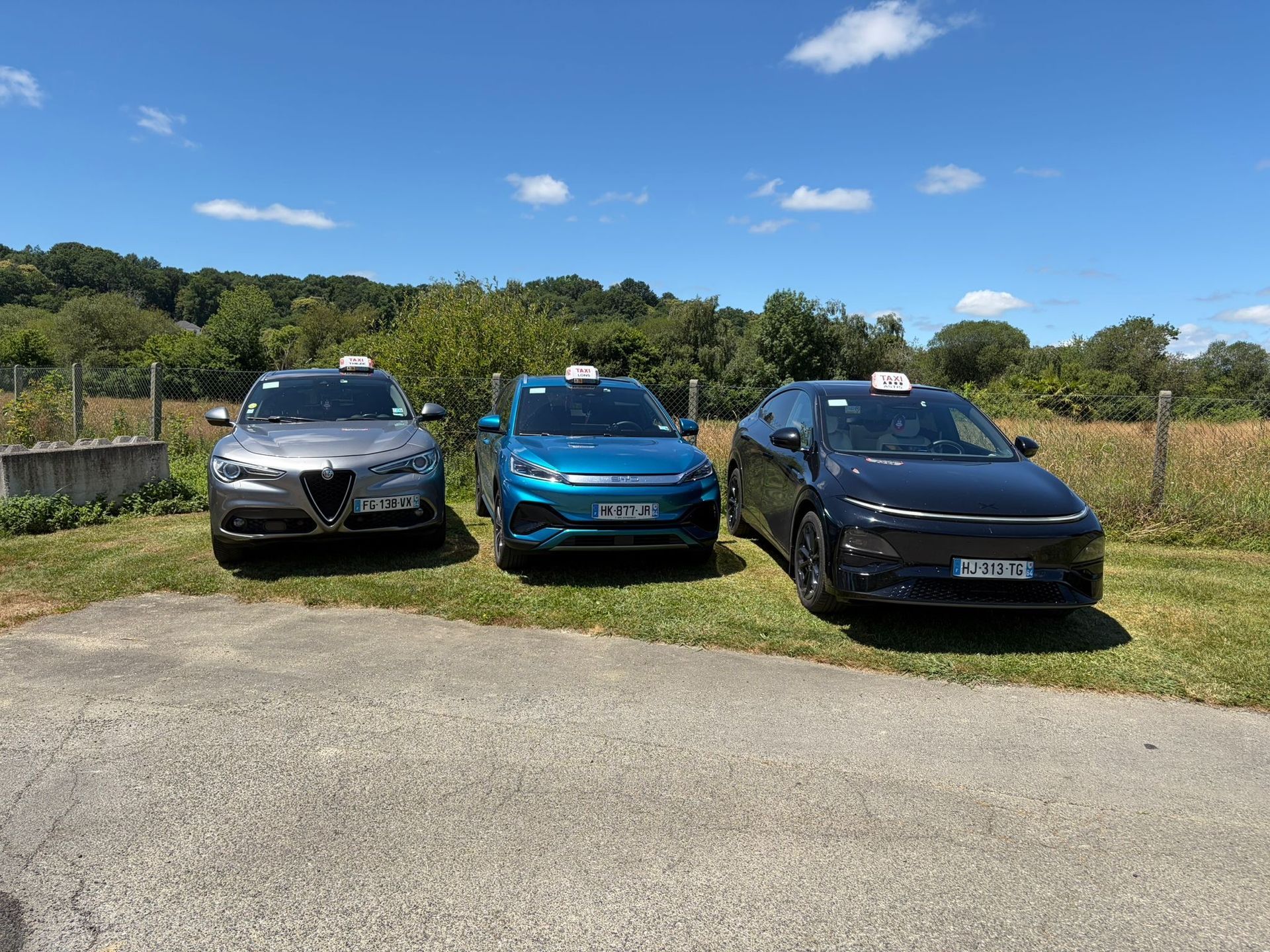 Trois SUV stationnés en bordure d'une route de campagne sous un ciel bleu, avec des arbres et de l'herbe en arrière-plan.