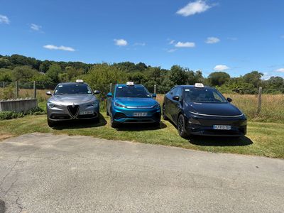 Trois voitures garées sur un parking ensoleillé en gravier, avec des arbres et un ciel bleu en arrière-plan.