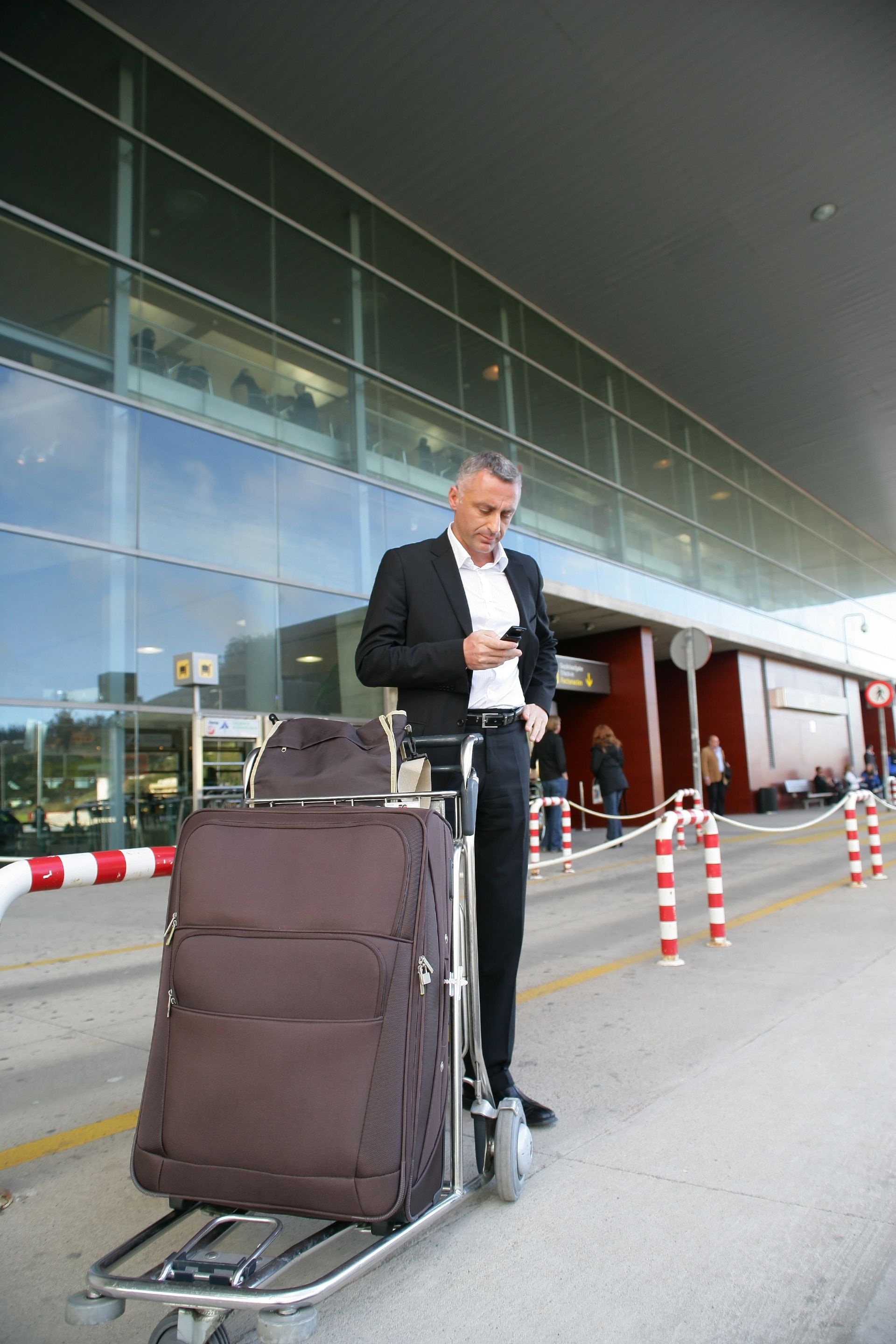 Un homme se tient debout avec un chariot à valises devant un terminal d'aéroport, sous une verrière.