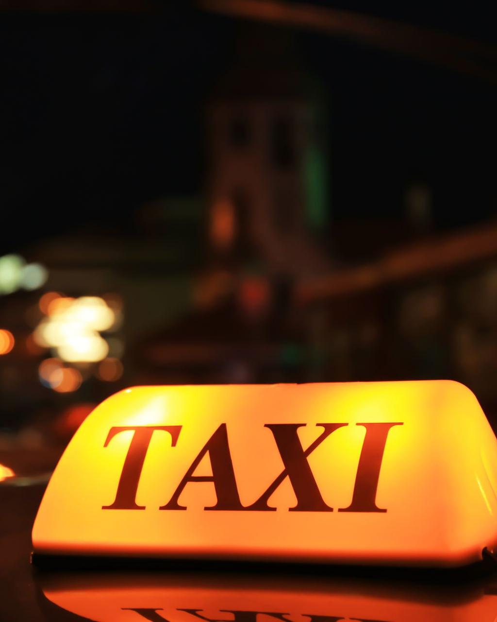 Panneau lumineux jaune de taxi se détachant sur un fond de rue nocturne sombre et flou.