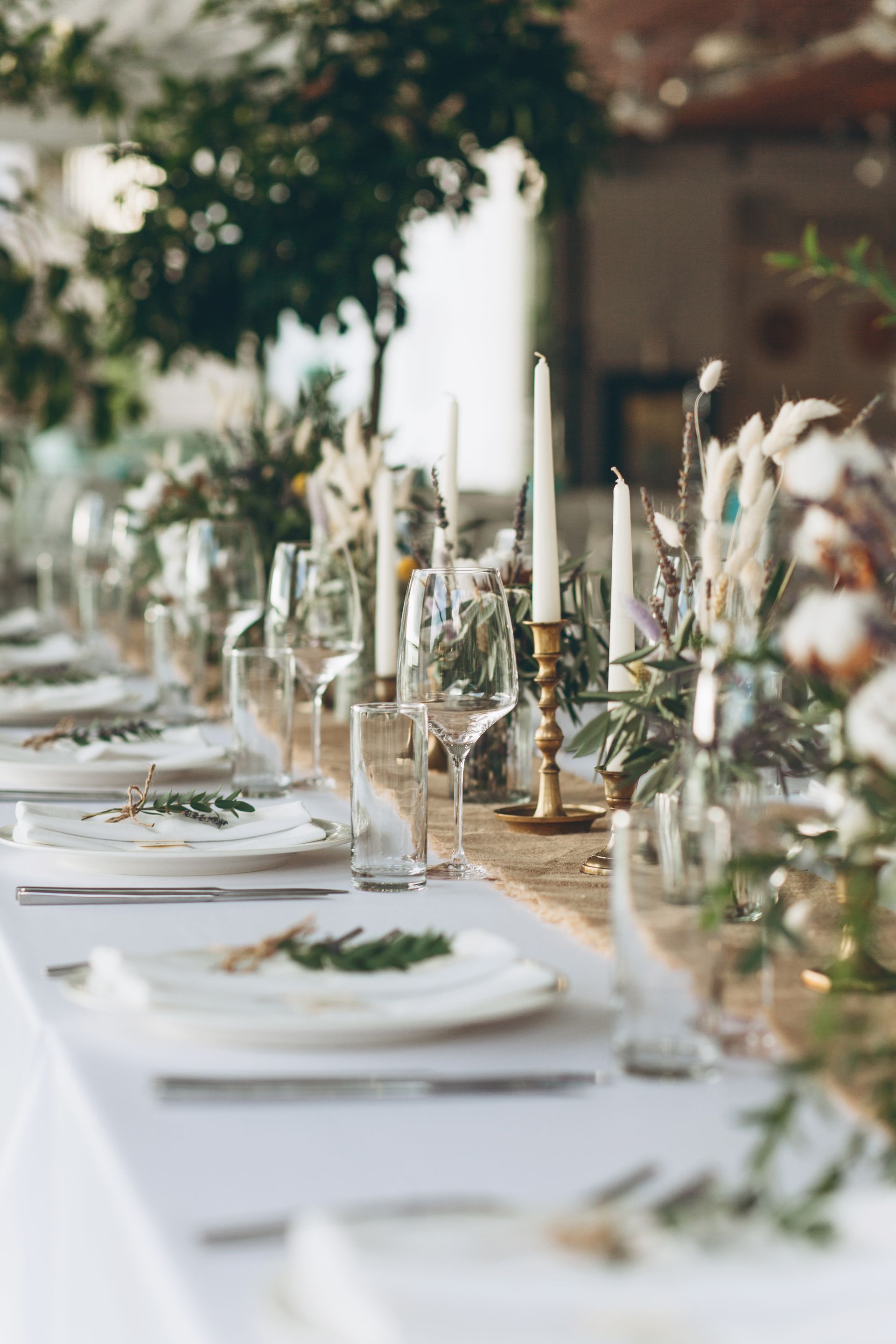 Élégante table à manger extérieure avec vaisselle blanche, bougies et verdure, dressée pour un événement.