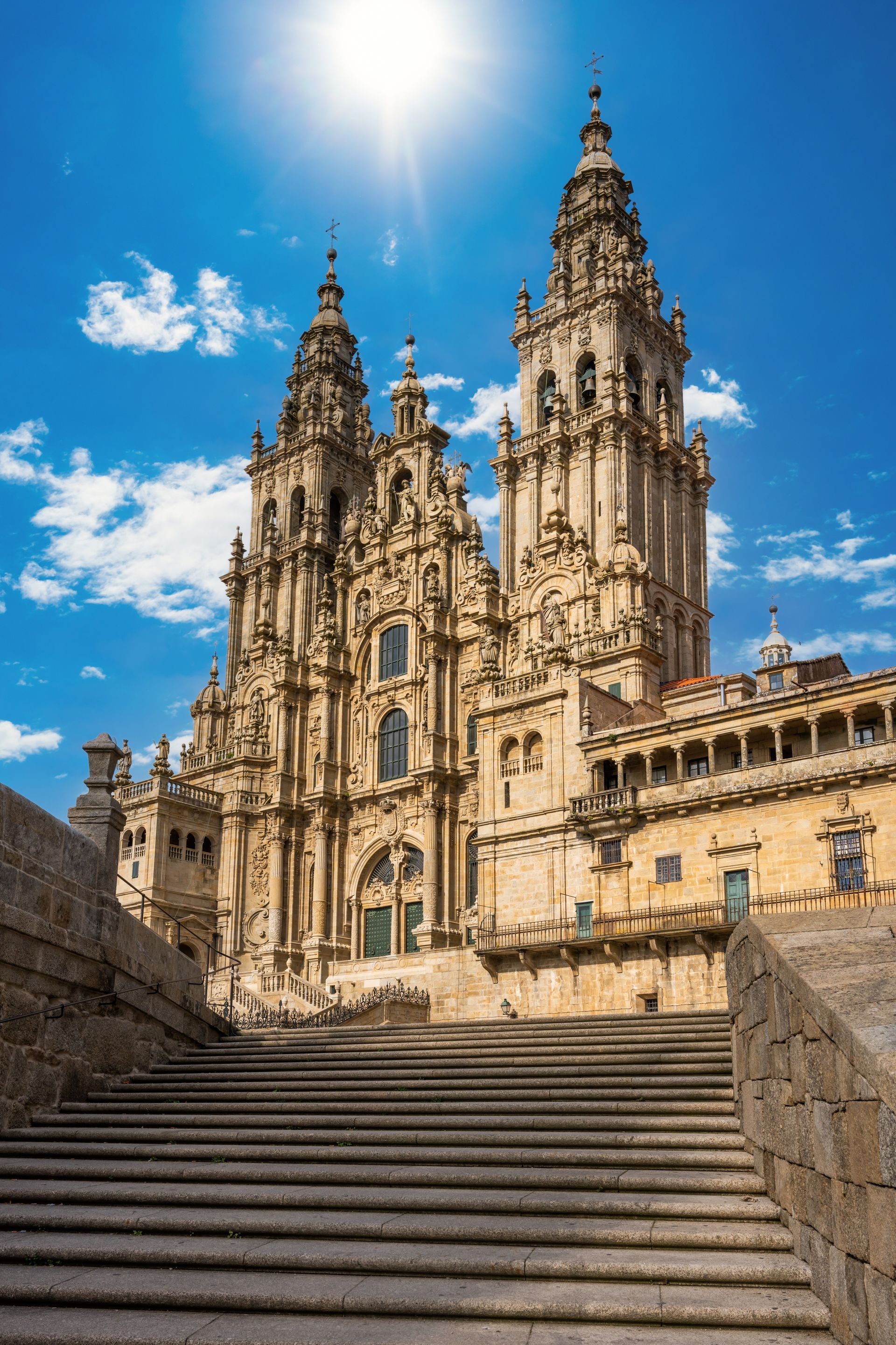 Cathédrale de pierre avec des tours jumelles au sommet de larges marches sous un ciel d'un bleu éclatant.