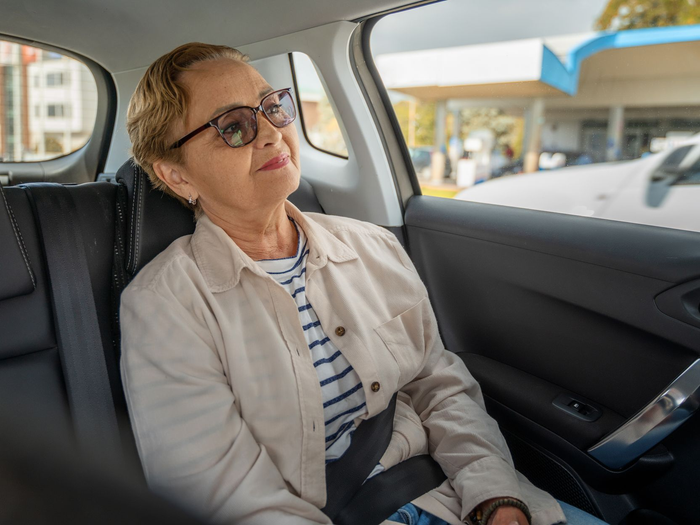 Une femme portant des lunettes est assise sur la banquette arrière d'une voiture, regardant par la fenêtre.