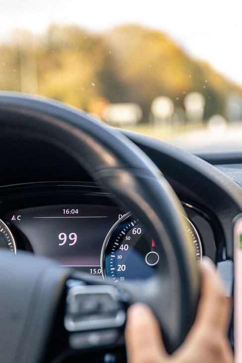 Main du conducteur sur le volant, tableau de bord numérique affichant 99 km/h sur fond de route floue.