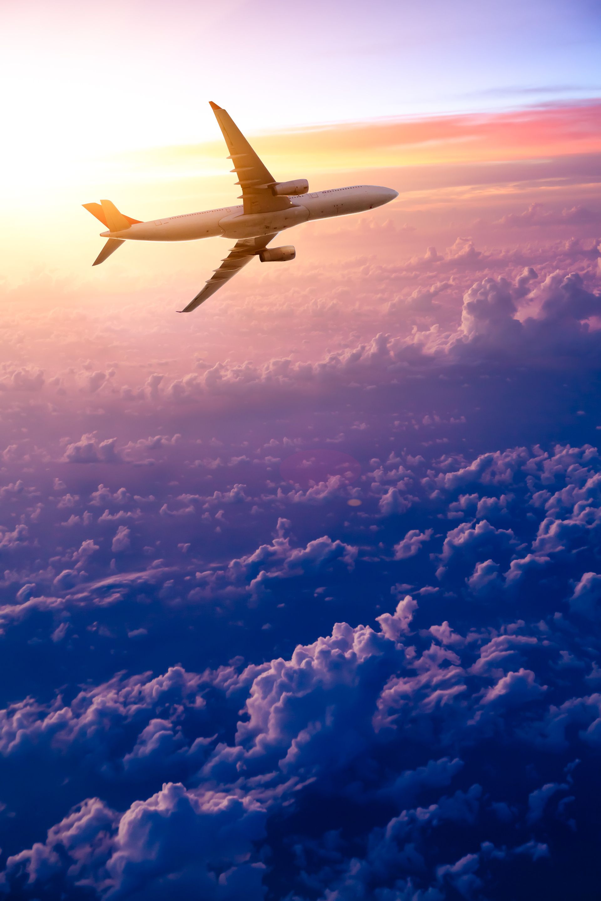 Avion volant au-dessus des nuages au lever du soleil, sous un ciel rose et doré.