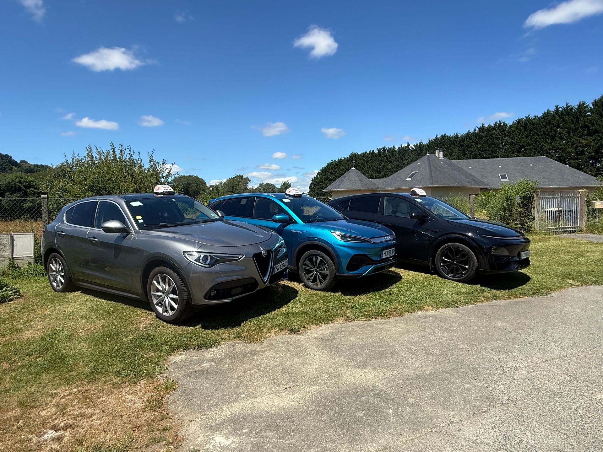 Trois SUV stationnés sur une allée herbeuse sous un ciel bleu près d'une maison