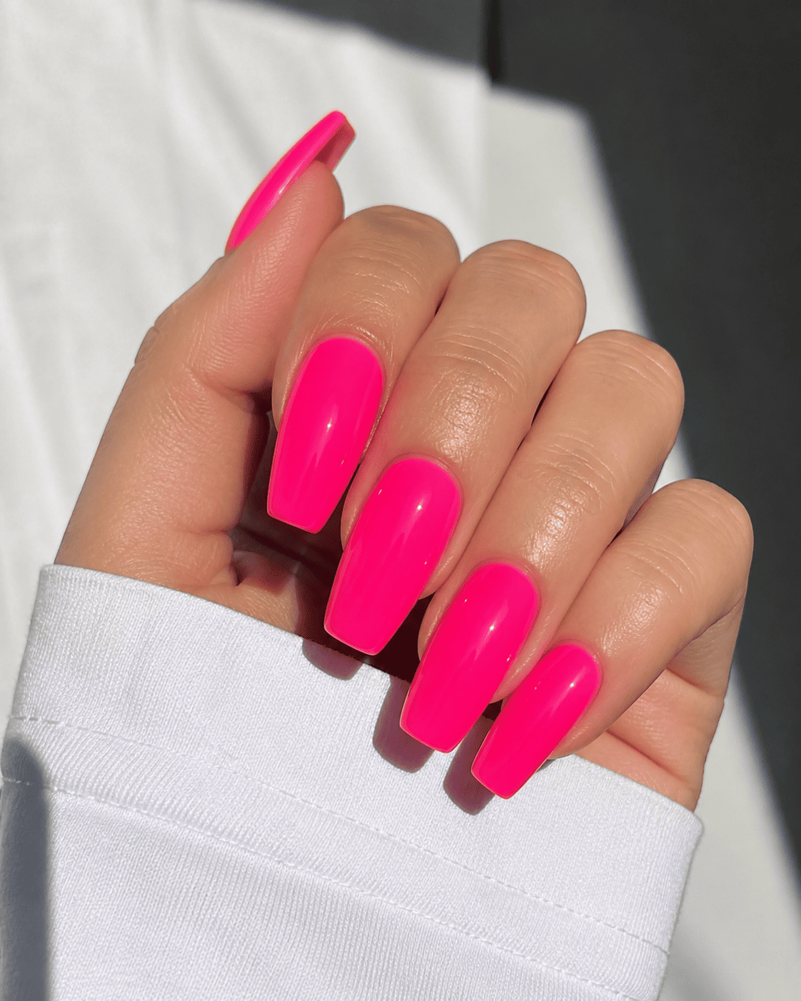Main aux longs ongles avec vernis rose vif.