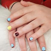 Deux mains aux ongles vernis bleu pastel, jaune et bordeaux foncé reposent côte à côte sur un fond rouge et blanc.