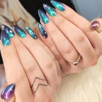 Des mains avec de longs ongles stilettos dégradés turquoise et violet et des tatouages ​​minimalistes.
