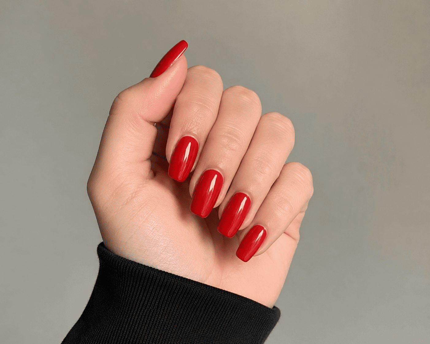 Main aux ongles rouges brillants sur fond gris, manche noire.