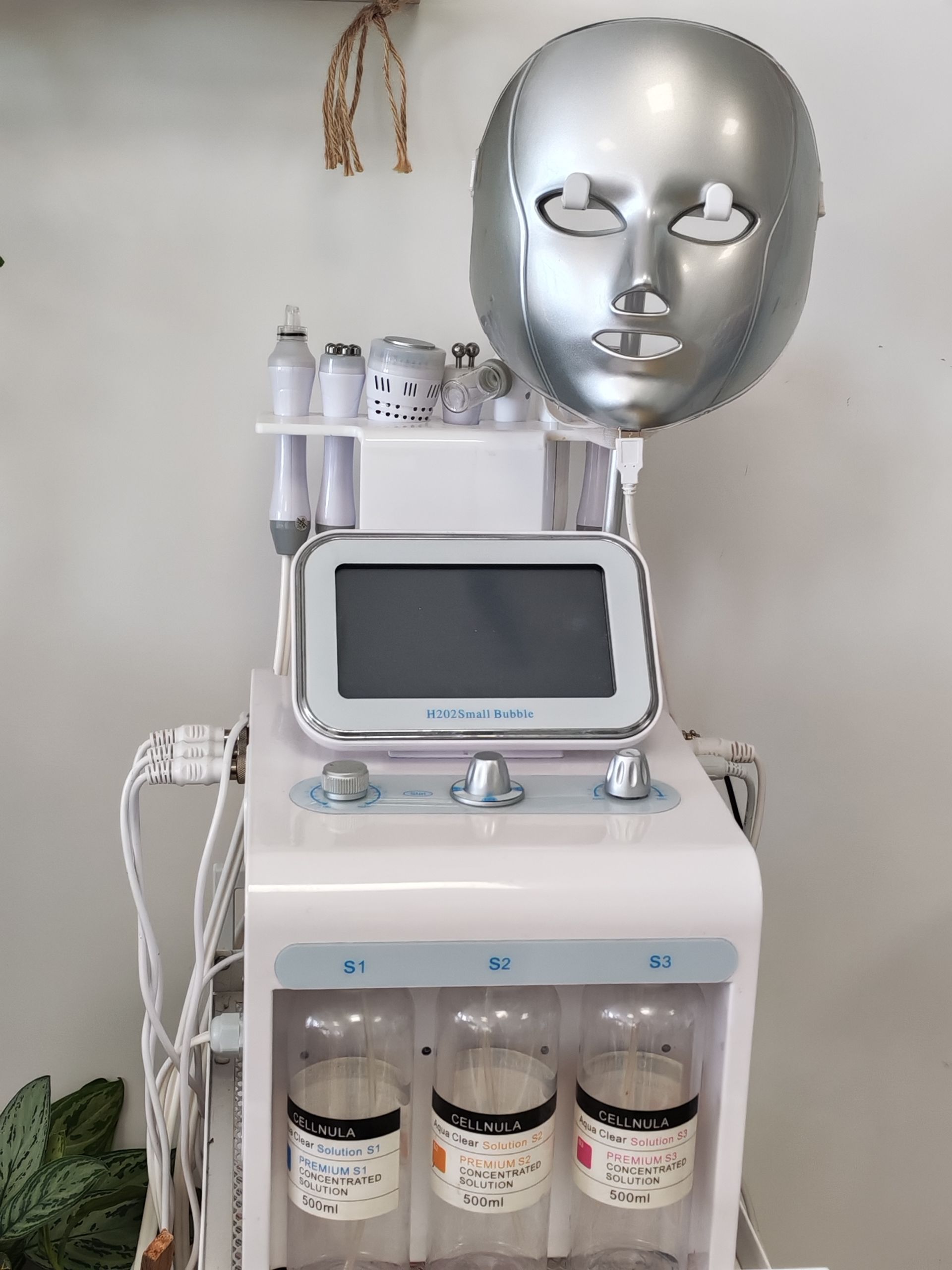 Appareil de soin du visage Hydrofacial avec masque argenté, écran et flacons, dans une pièce de l'institut.