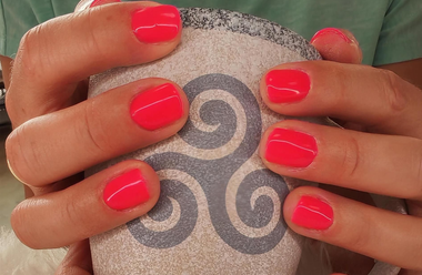 Des mains aux ongles corail rose vif tiennent une tasse en granit avec le triskèle breton.