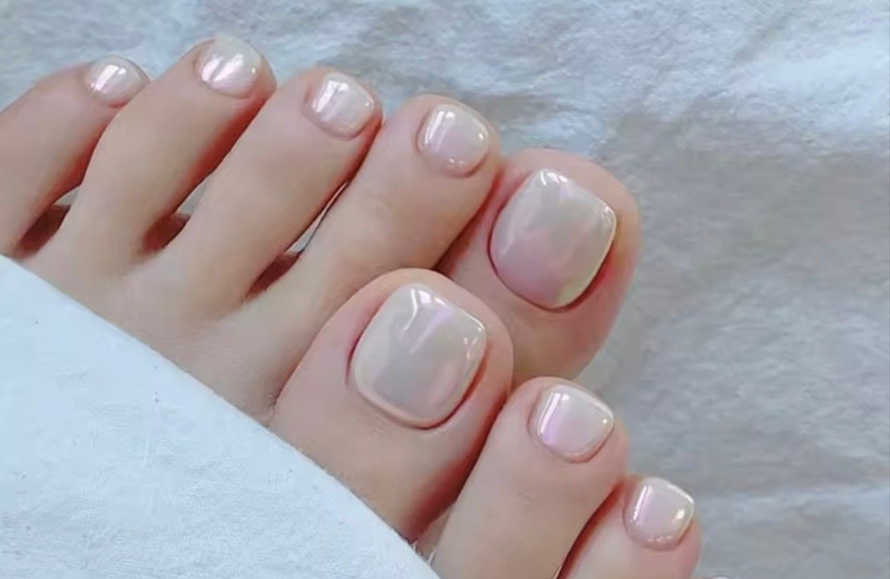 Gros plan sur des orteils nus vernis à ongles rose pâle, posés sur une douce couverture blanche.