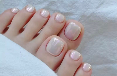 Gros plan sur des pieds nus aux ongles de pieds vernis rose pâle, posés sur une douce couverture blanche.