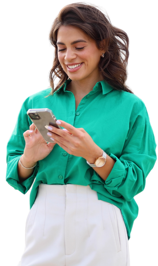 Femme souriante en chemise verte regardant un smartphone à l'extérieur.