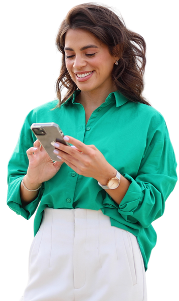 Femme souriante en chemise verte regardant un smartphone à l'extérieur.