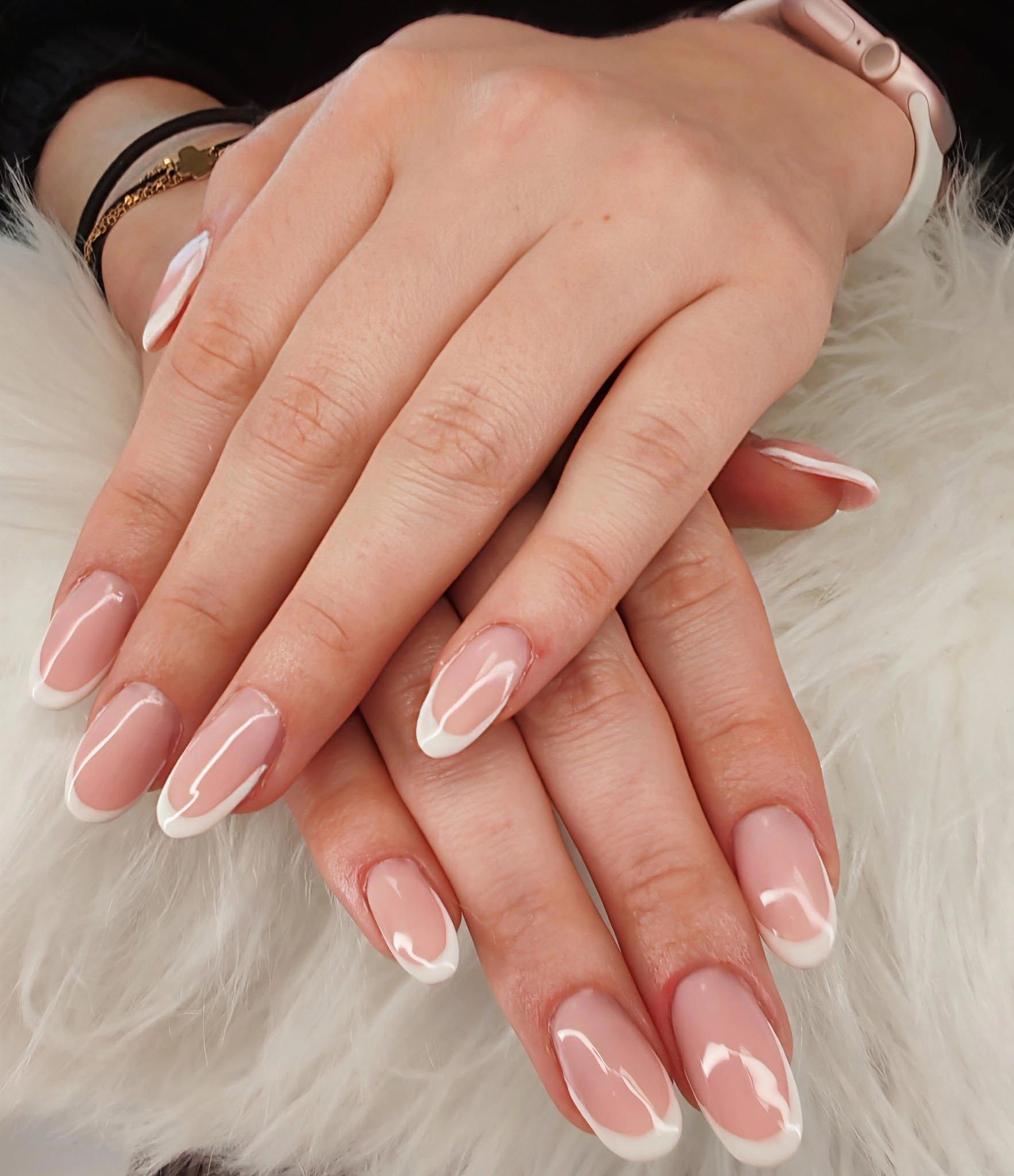 Gros plan sur des mains manucurées aux ongles rose pâle vernis à la française, posées sur de la fourrure blanche.