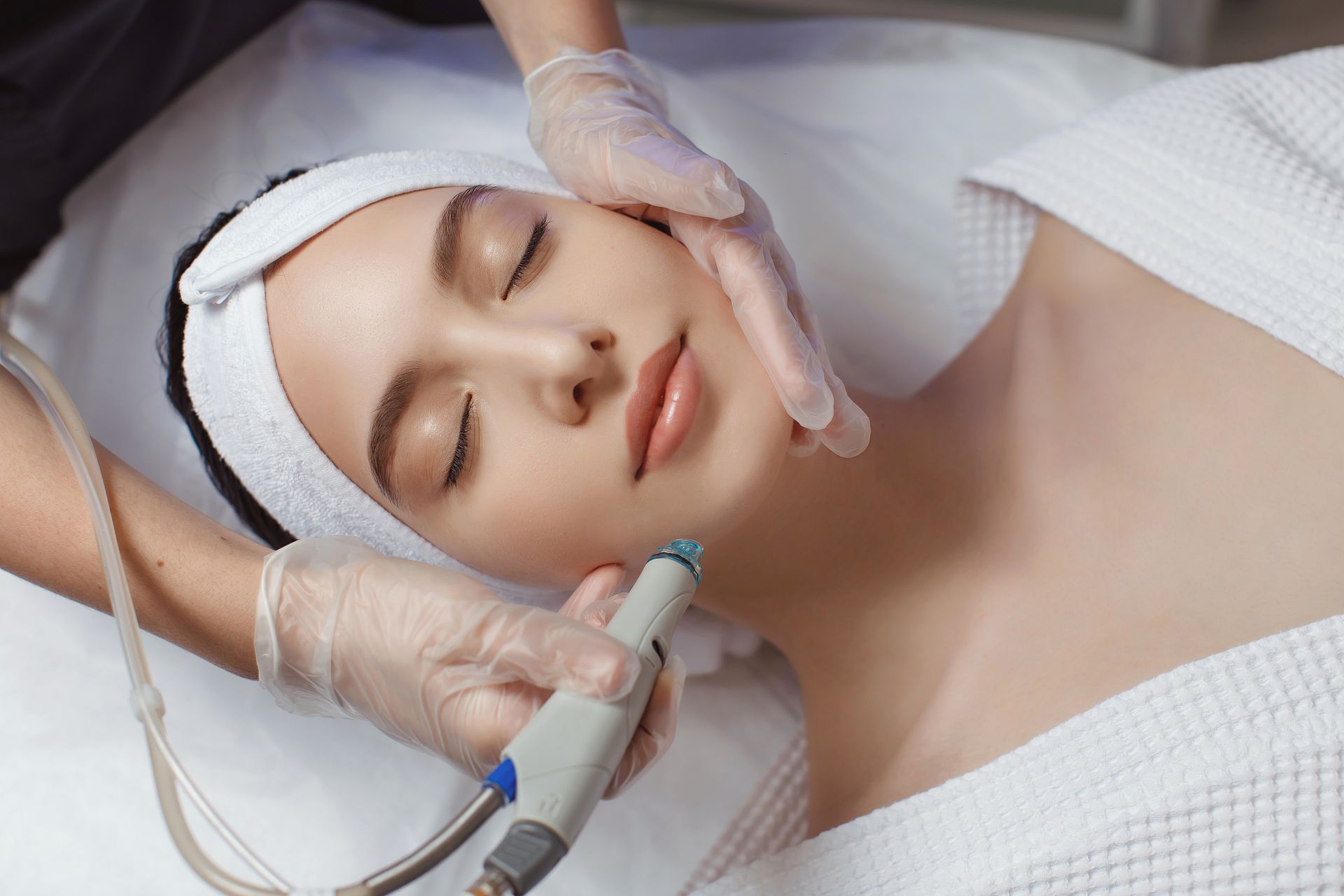 Soin du visage sur une femme allongée, les mains gantées utilisant un appareil de soin sur son menton.