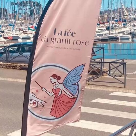 Drapeau publicitaire avec inscription La Fée du Granit Rose près du port de plaisance avec des bateaux en arrière-plan.