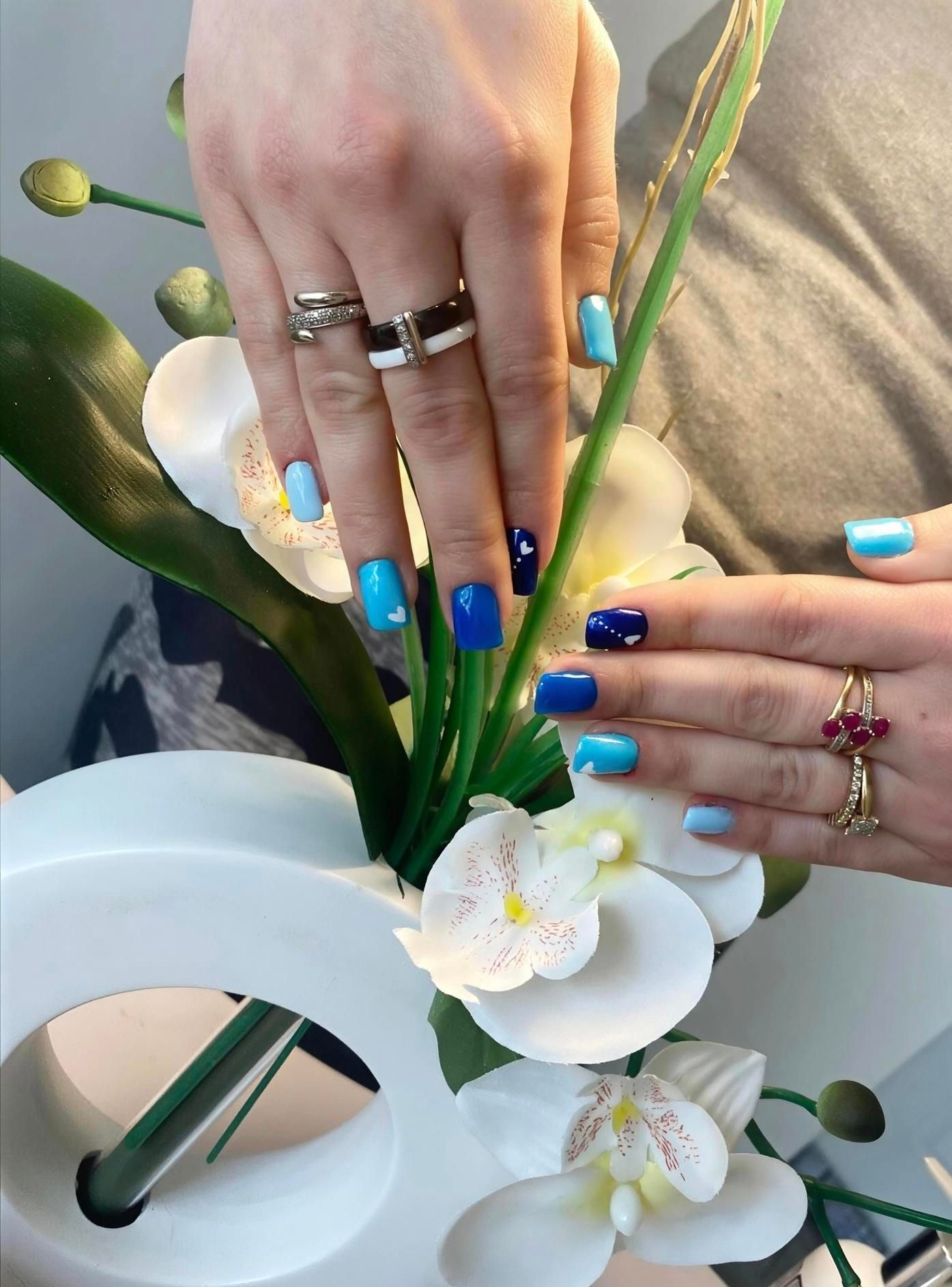 Des mains arrangent des fleurs blanches dans un vase blanc avec des touches de bleu.