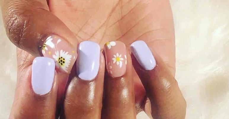 Gros plan sur des mains manucurées avec des ongles lavande pastel et des motifs floraux blancs.