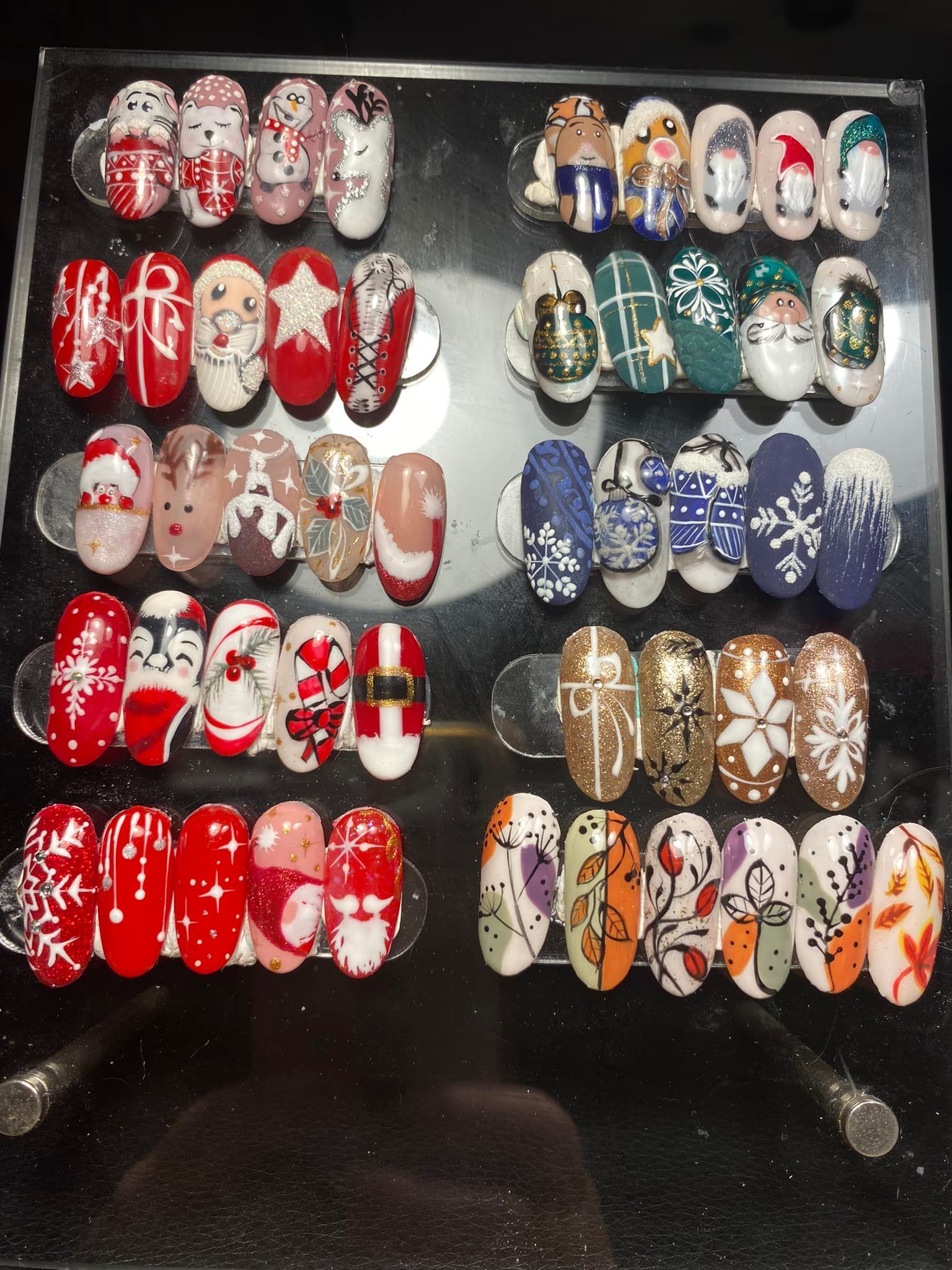 Des rangées de faux ongles décoratifs colorés, ornés de motifs sur le thème des fêtes, présentées sur un panneau.