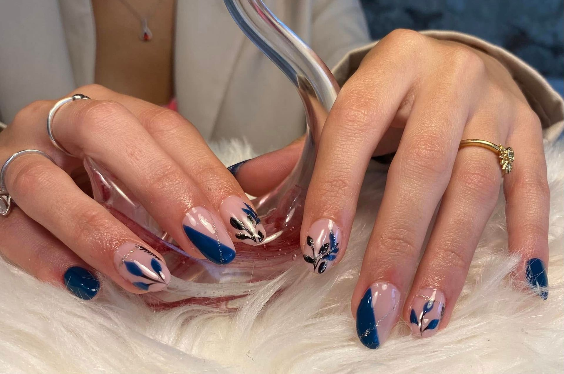 Des mains aux longs ongles manucurés bleus, blancs et fleuris, posées sur une surface blanche et duveteuse.