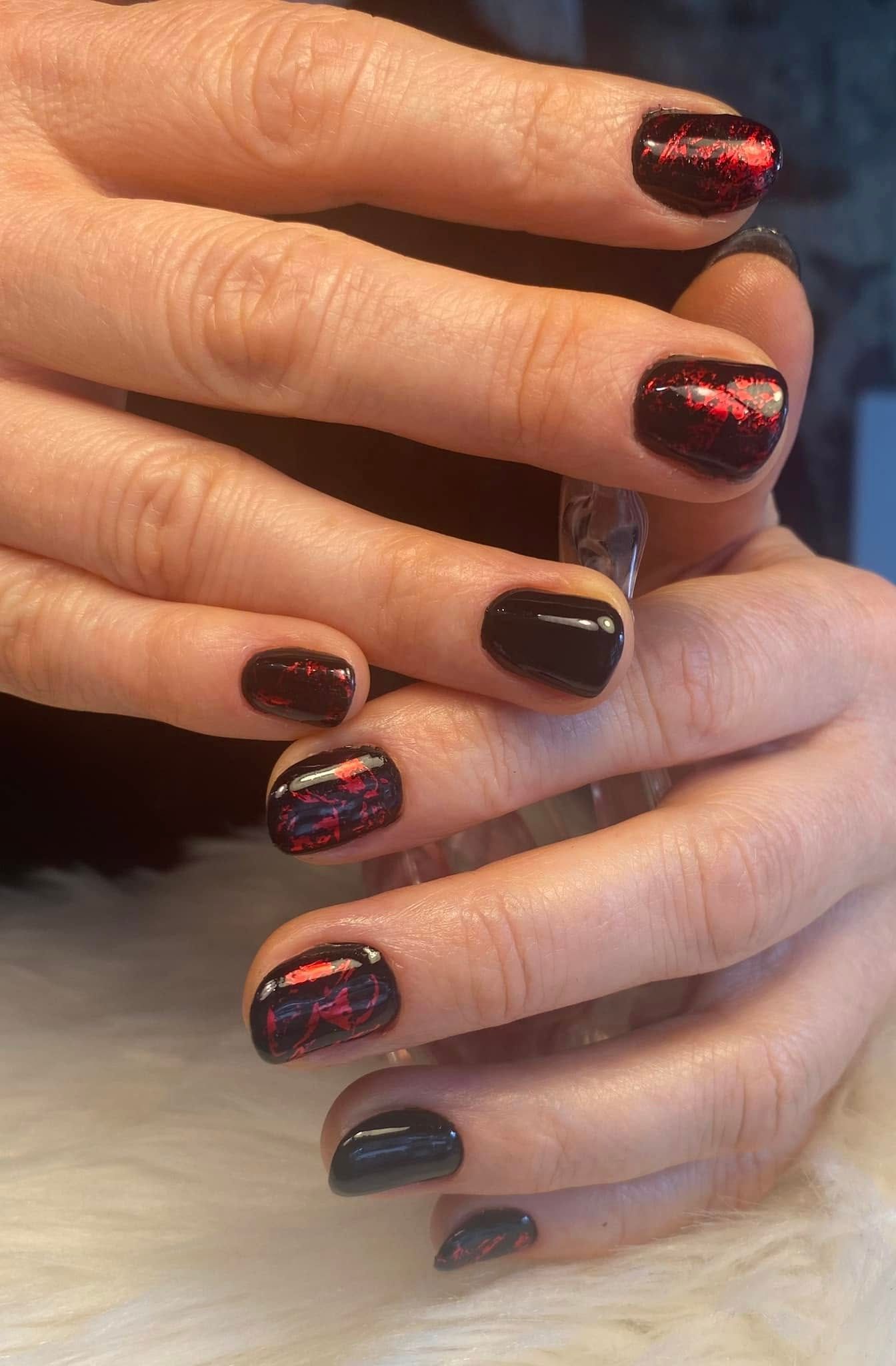 Gros plan sur des mains avec une manucure pailletée bordeaux foncé et rouge et des ongles noirs brillants.
