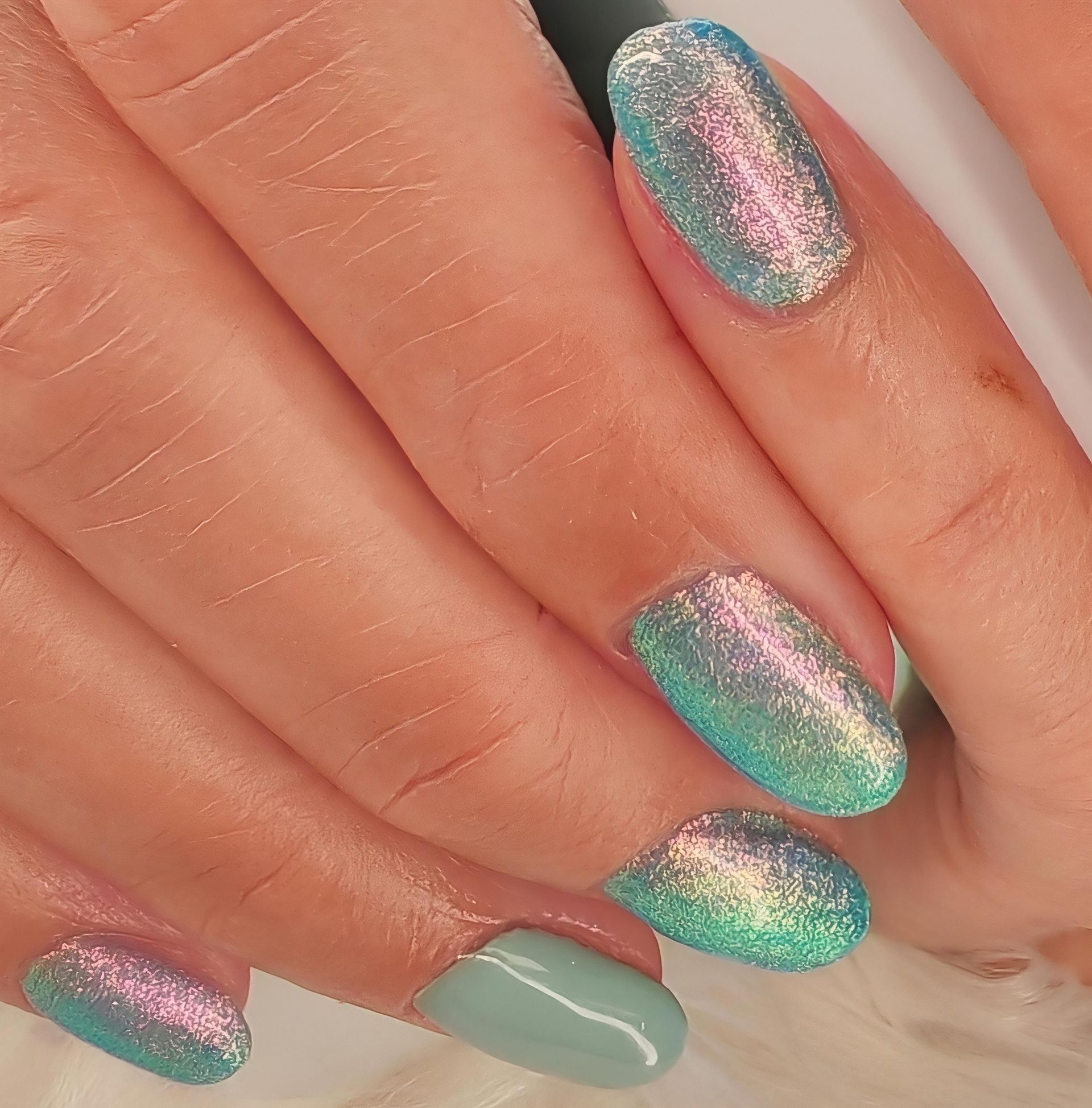 Main avec des ongles manucurés vert pastel et rose irisé pailleté.