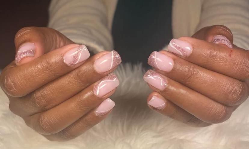 Deux mains aux ongles vernis rose pâle brillants, jointes sur un fond blanc doux.
