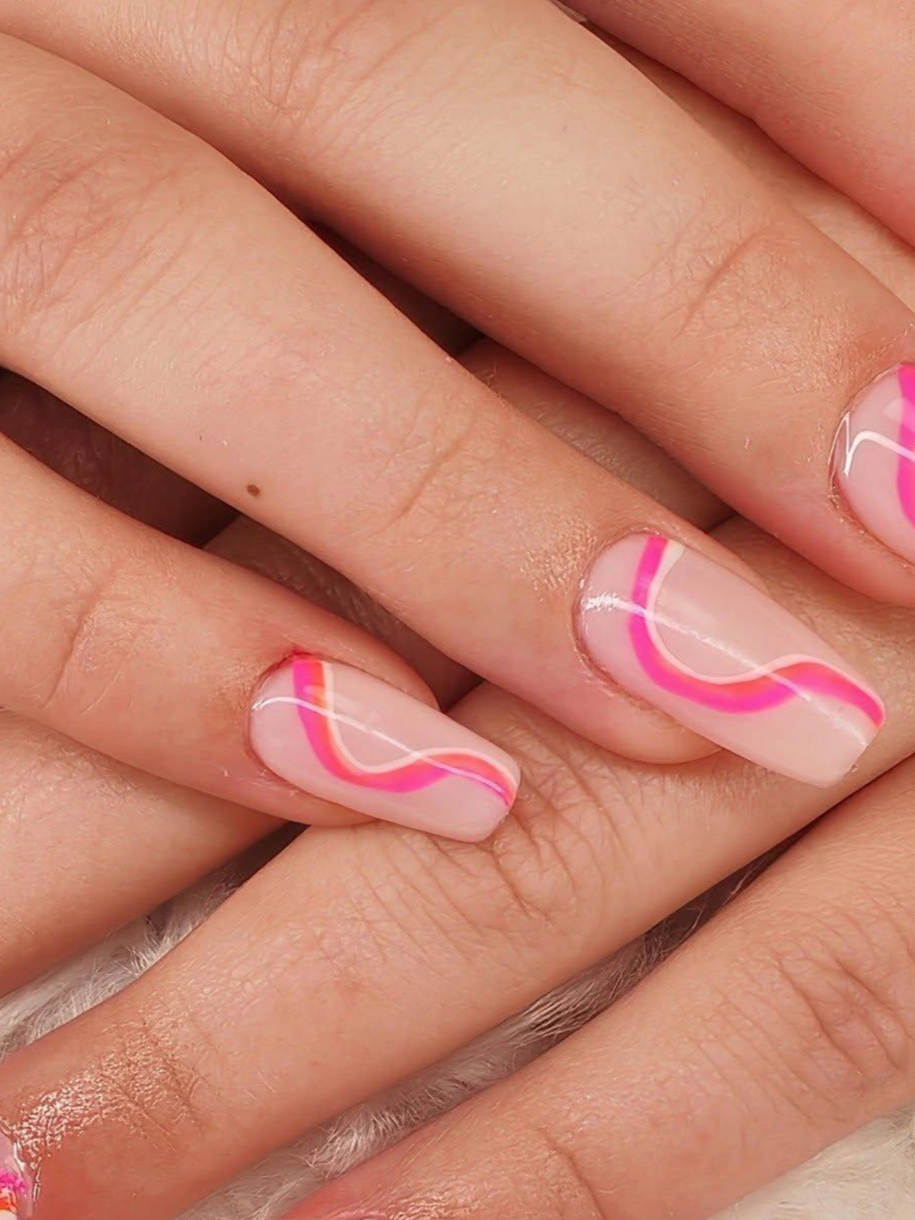 Gros plan sur des mains avec une manucure ondulée rose et blanche sur des ongles nude.