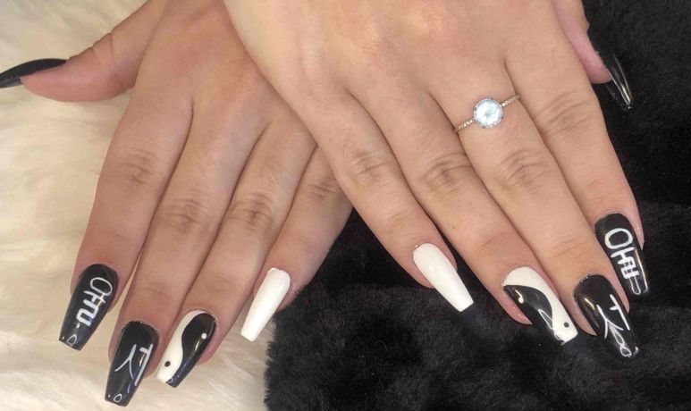Des mains aux longs ongles noirs et blancs sont présentées sur une surface sombre, l'une d'elles portant une bague.