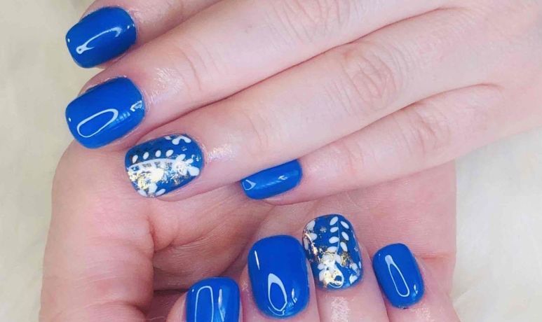 Gros plan sur des mains aux ongles manucurés d'un bleu vif, certaines ornées de motifs floraux blancs.