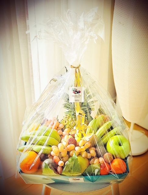 Panier-cadeau de fruits frais assortis, emballé dans du cellophane transparent et orné d'un ruban.