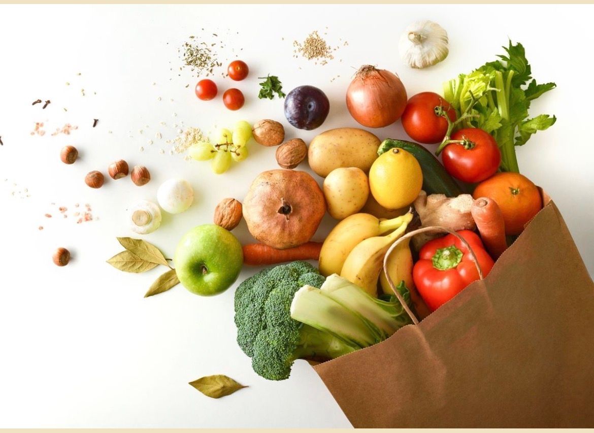 Sac en papier brun déversant un assortiment de fruits et légumes frais sur fond blanc